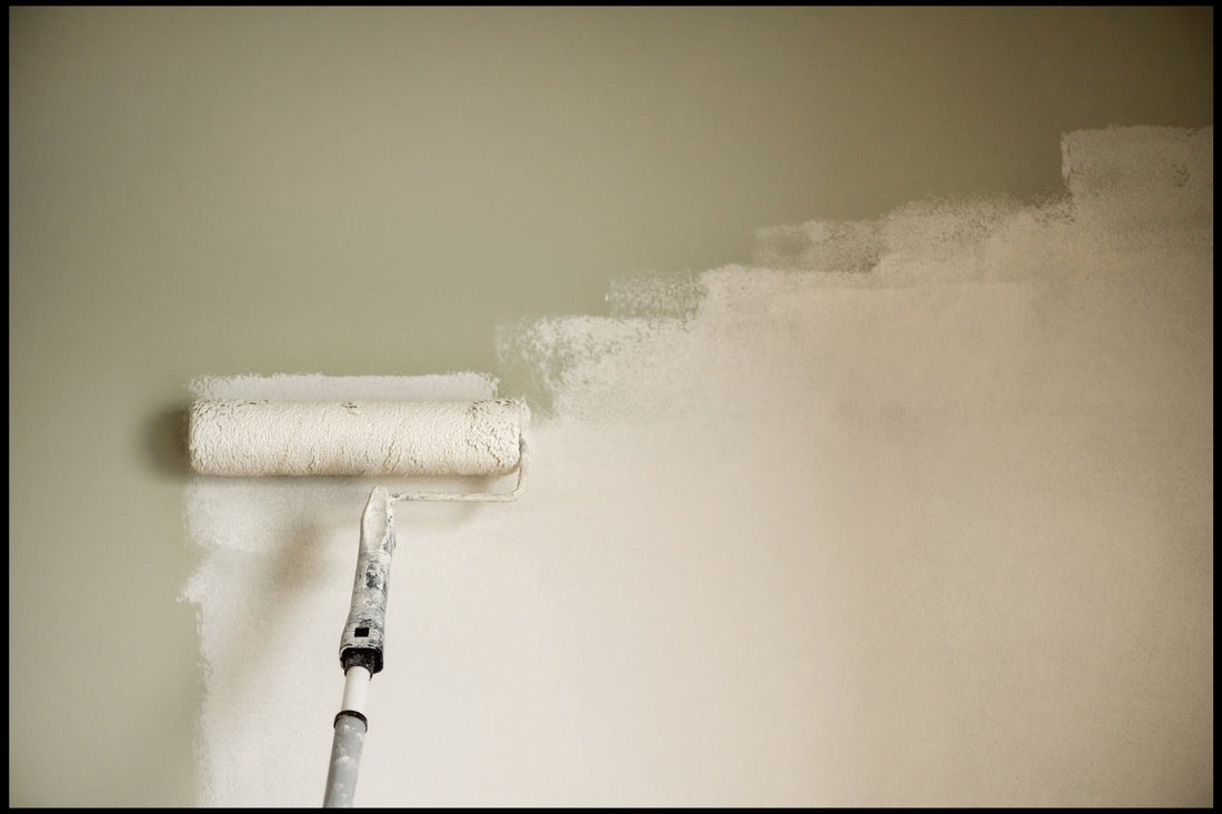 Professional decorator applying paint to a wall using a long roller pole and full-size roller sleeve, creating an even first coat.