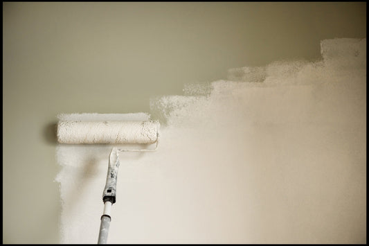 Professional decorator applying paint to a wall using a long roller pole and full-size roller sleeve, creating an even first coat.